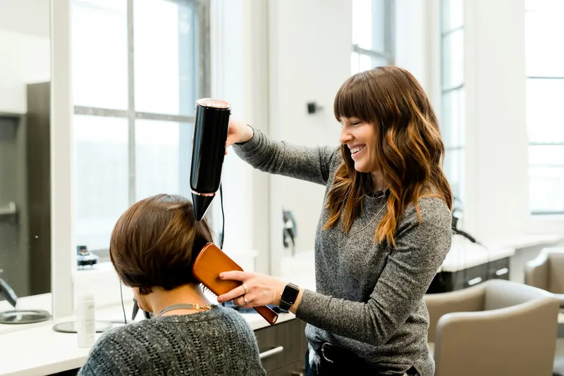 Coiffeuse souriante qui fait un brushing à une cliente dans un salon lumineux