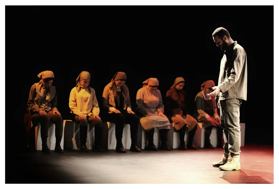 Un comédien d'improvisation debout face à une rangée de comédiens assis sur une scène noire