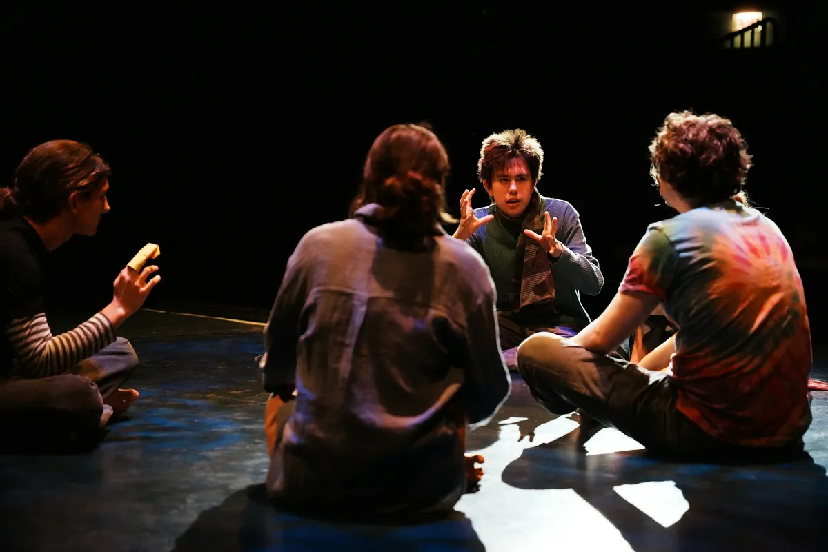 Quatre comédiens d'improvisation assis sur une scène noire, sous un projecteur