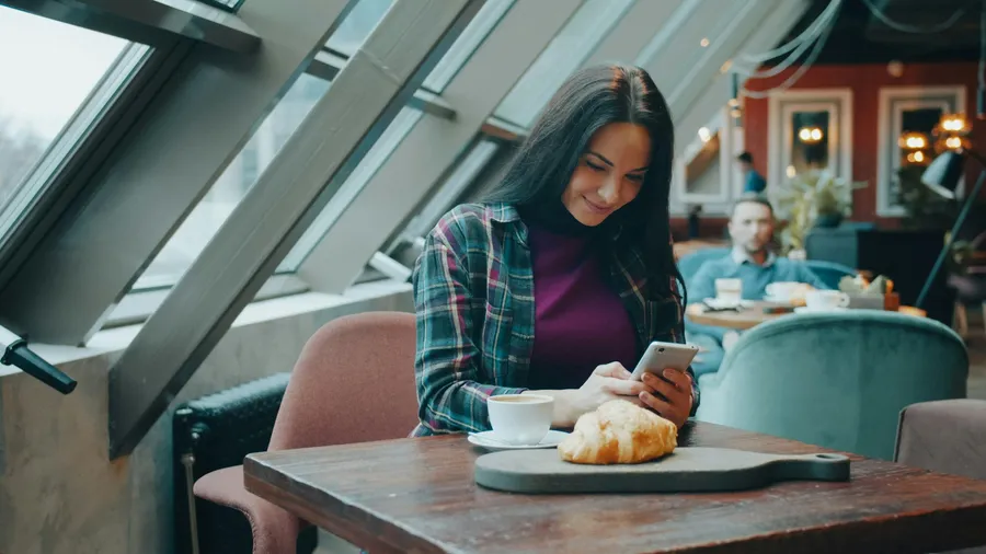 Femme souriante qui consulte une application sur son téléphone dans un café